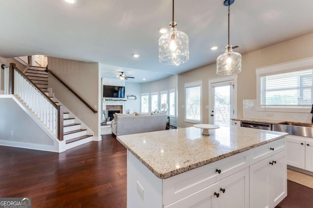 kitchen featuring ceiling fan, a center island, a stone fireplace, pendant lighting, and white cabinets