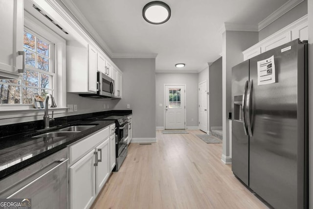 kitchen featuring dark stone counters, stainless steel appliances, crown molding, sink, and white cabinetry