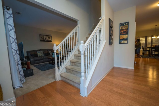 stairway featuring wood-type flooring and an inviting chandelier