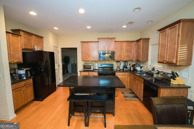 kitchen featuring light wood-type flooring, a center island, tasteful backsplash, and black appliances