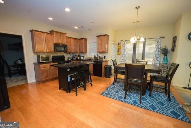 kitchen featuring a kitchen bar, light wood-type flooring, black appliances, an inviting chandelier, and a center island