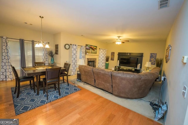 living room featuring ceiling fan with notable chandelier, hardwood / wood-style flooring, and a tiled fireplace