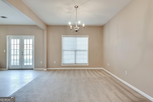 empty room with light carpet, french doors, a textured ceiling, and an inviting chandelier