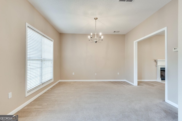 carpeted spare room featuring a textured ceiling, an inviting chandelier, and a healthy amount of sunlight