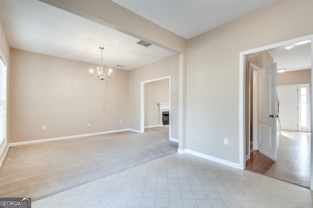 unfurnished room with a textured ceiling, light colored carpet, and an inviting chandelier