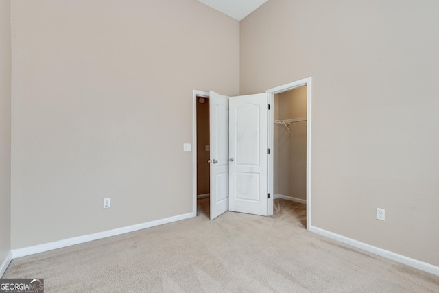 unfurnished bedroom featuring light colored carpet, a spacious closet, a high ceiling, and a closet