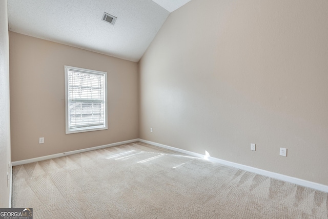 spare room with a textured ceiling, light carpet, and vaulted ceiling