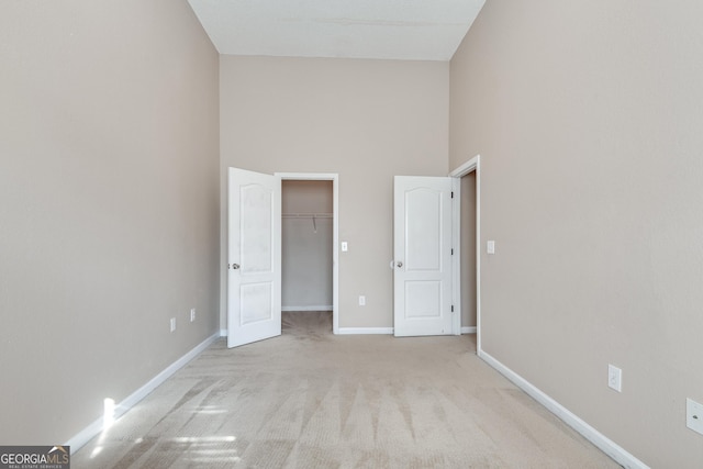 unfurnished bedroom featuring light carpet, a high ceiling, a spacious closet, and a closet