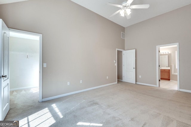 unfurnished bedroom with ceiling fan, a walk in closet, light carpet, and high vaulted ceiling