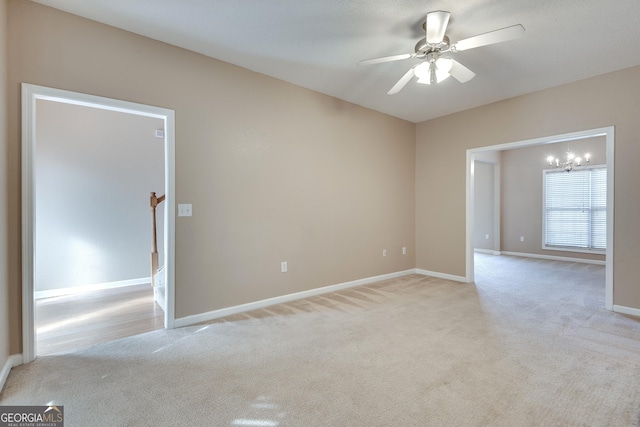 empty room with ceiling fan with notable chandelier and light colored carpet