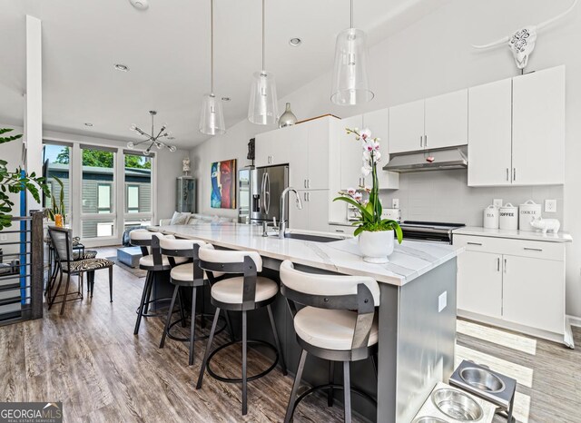 kitchen with backsplash, a center island with sink, stainless steel fridge with ice dispenser, white cabinetry, and hanging light fixtures