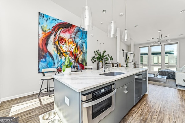 kitchen featuring stainless steel appliances, a sink, open floor plan, gray cabinets, and a center island with sink