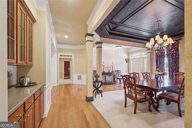 dining space with light hardwood / wood-style floors, ornate columns, crown molding, and an inviting chandelier