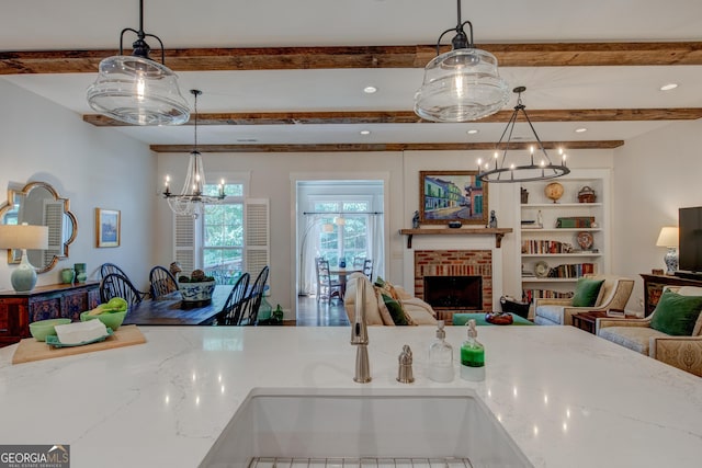 kitchen with pendant lighting, sink, a brick fireplace, built in features, and light stone counters