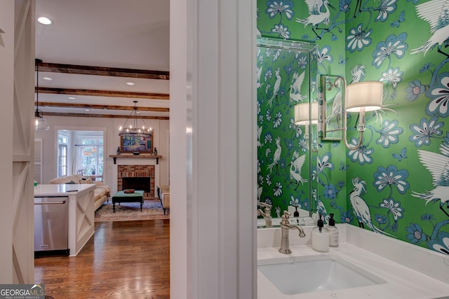 bathroom with a fireplace, vanity, hardwood / wood-style flooring, a notable chandelier, and beamed ceiling