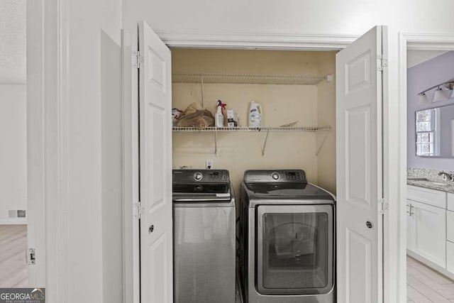 laundry area featuring washing machine and dryer, sink, and light hardwood / wood-style flooring