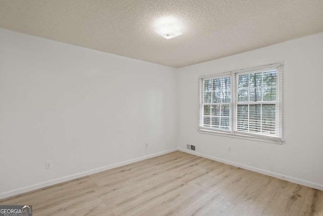 empty room with light hardwood / wood-style floors and a textured ceiling