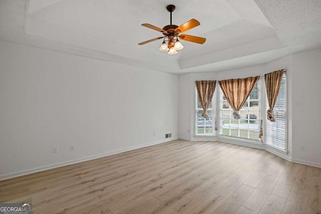 spare room featuring a raised ceiling, ceiling fan, and light hardwood / wood-style flooring