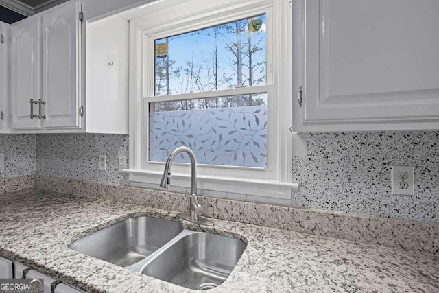 kitchen with white cabinets, backsplash, light stone countertops, and sink