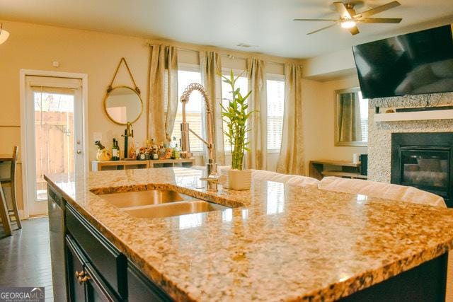 kitchen featuring ceiling fan, a healthy amount of sunlight, light stone countertops, and sink