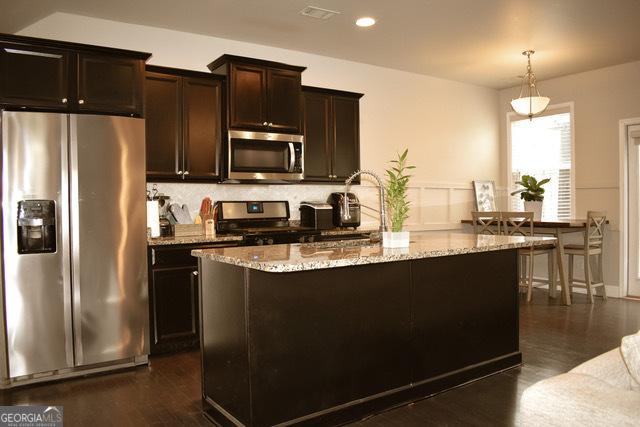 kitchen featuring light stone countertops, dark brown cabinets, stainless steel appliances, sink, and pendant lighting