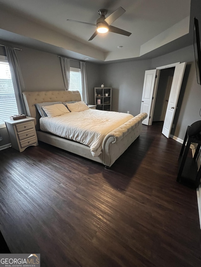 bedroom with dark hardwood / wood-style flooring, a tray ceiling, and ceiling fan