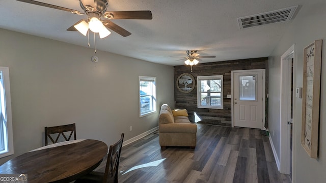 interior space with ceiling fan, dark wood-type flooring, a textured ceiling, and wood walls