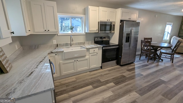 kitchen featuring white cabinetry, sink, light stone counters, light hardwood / wood-style floors, and stainless steel appliances