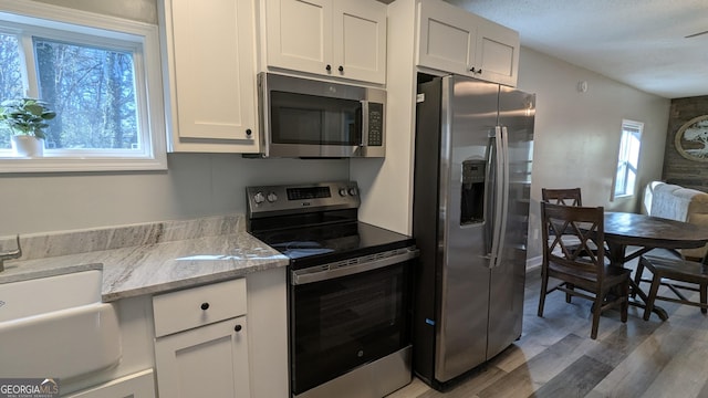 kitchen featuring hardwood / wood-style floors, sink, white cabinets, stainless steel appliances, and light stone countertops