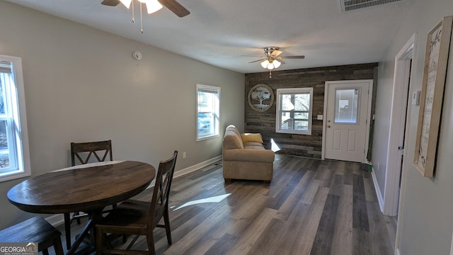 dining space with dark hardwood / wood-style floors, ceiling fan, wooden walls, and a textured ceiling