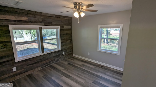 unfurnished room featuring dark hardwood / wood-style flooring, a textured ceiling, ceiling fan, and wood walls