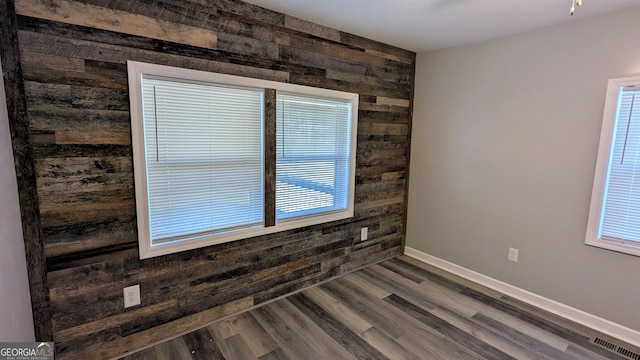 unfurnished room with hardwood / wood-style flooring, a healthy amount of sunlight, and wooden walls