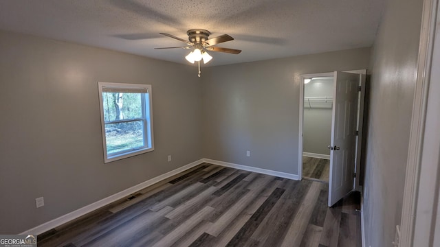 unfurnished bedroom with a walk in closet, a textured ceiling, dark hardwood / wood-style floors, a closet, and ceiling fan