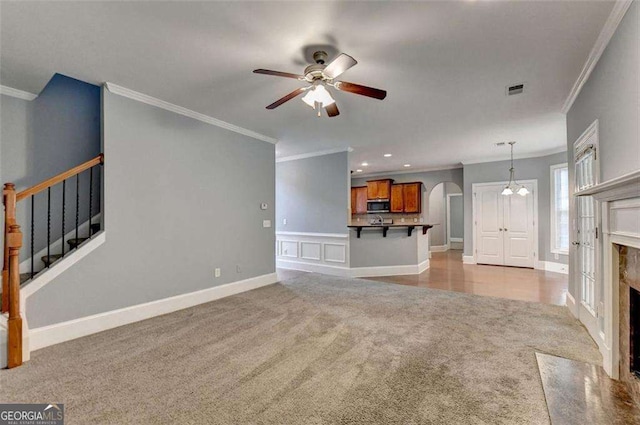 unfurnished living room featuring ceiling fan, light colored carpet, crown molding, and a high end fireplace