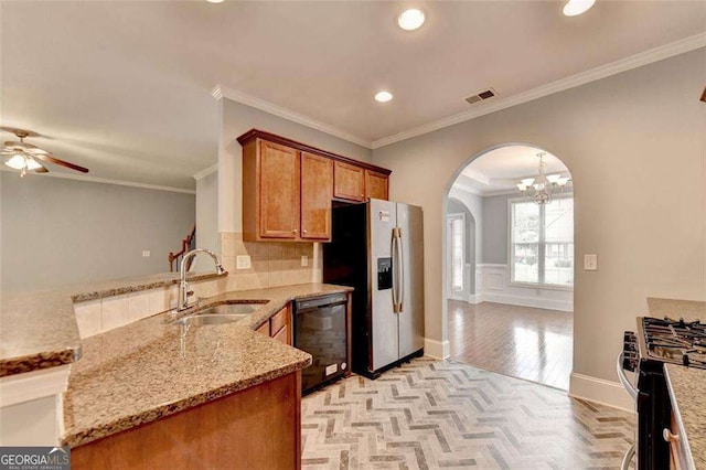 kitchen with ceiling fan with notable chandelier, sink, ornamental molding, light stone counters, and stainless steel appliances