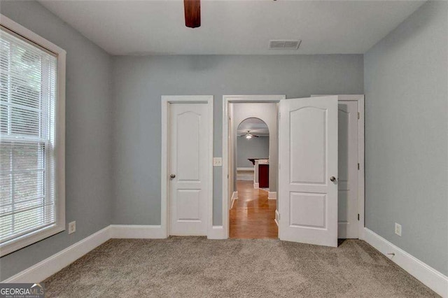 unfurnished bedroom featuring light carpet, multiple windows, and ceiling fan