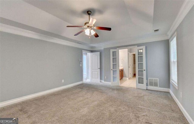 unfurnished bedroom featuring connected bathroom, ceiling fan, french doors, a raised ceiling, and ornamental molding