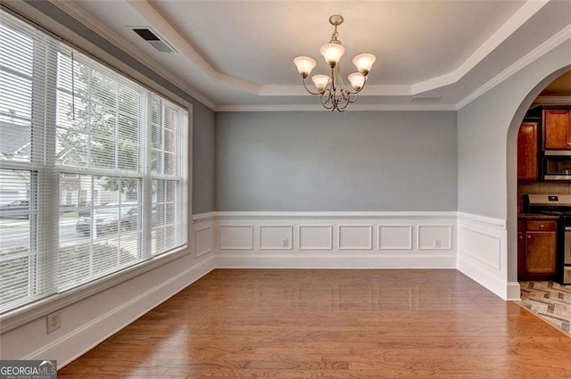 unfurnished dining area with hardwood / wood-style flooring, an inviting chandelier, crown molding, and a tray ceiling