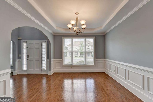 entrance foyer with hardwood / wood-style flooring, a notable chandelier, a raised ceiling, and ornamental molding