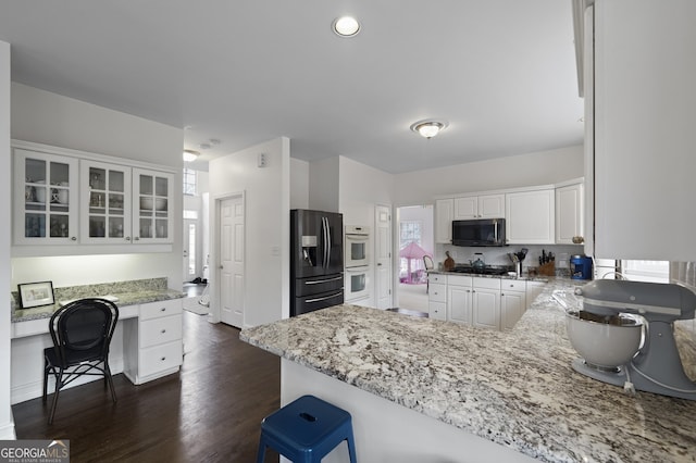 kitchen with black fridge, kitchen peninsula, double oven, light stone counters, and white cabinetry