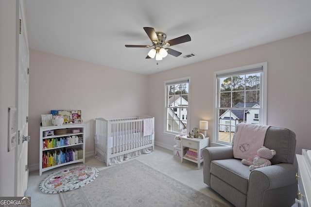 bedroom with a crib, light colored carpet, and ceiling fan