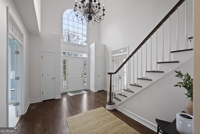 foyer with dark hardwood / wood-style flooring, a towering ceiling, and a notable chandelier