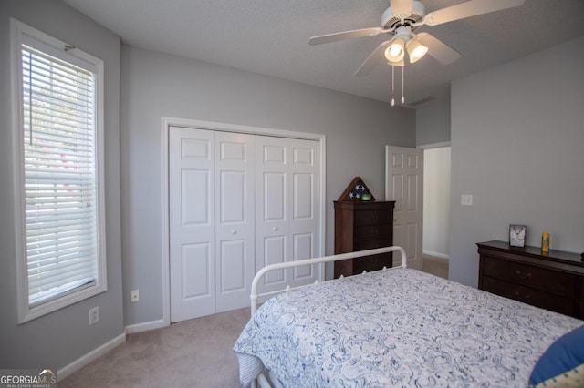 bedroom with a textured ceiling, a closet, ceiling fan, and light colored carpet