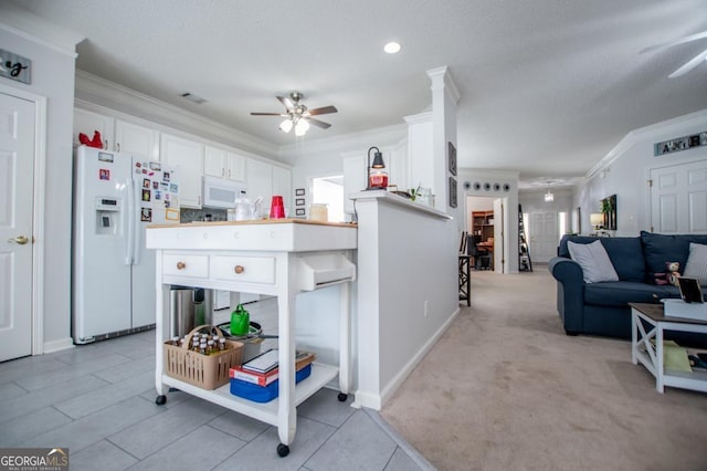 kitchen featuring kitchen peninsula, white appliances, light colored carpet, ceiling fan, and white cabinets