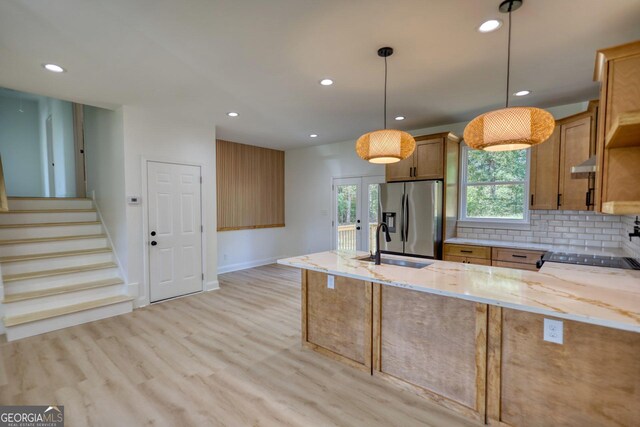 kitchen featuring sink, kitchen peninsula, light stone countertops, decorative light fixtures, and stainless steel fridge with ice dispenser