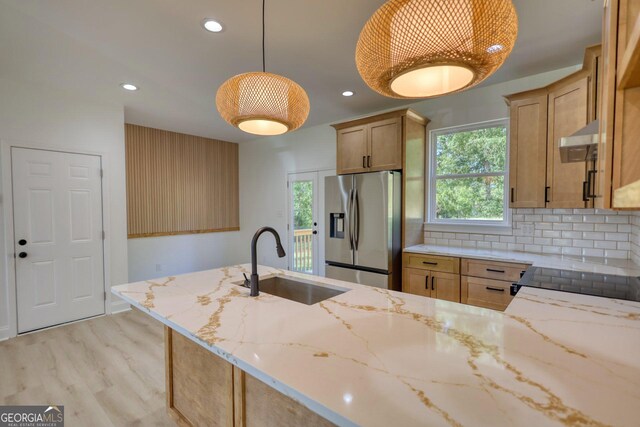 kitchen with light stone countertops, stainless steel fridge, light brown cabinetry, sink, and pendant lighting