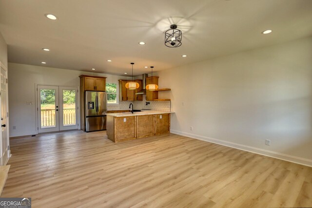 kitchen with wall chimney range hood, light hardwood / wood-style flooring, stainless steel refrigerator with ice dispenser, kitchen peninsula, and decorative light fixtures