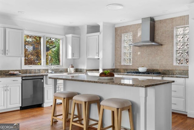 kitchen featuring white cabinets, a center island, wall chimney exhaust hood, and stainless steel appliances