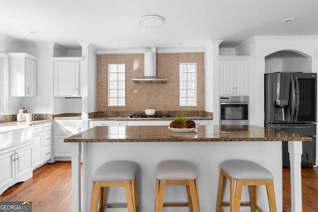 kitchen with white cabinetry, dark stone countertops, wall chimney range hood, and stainless steel appliances