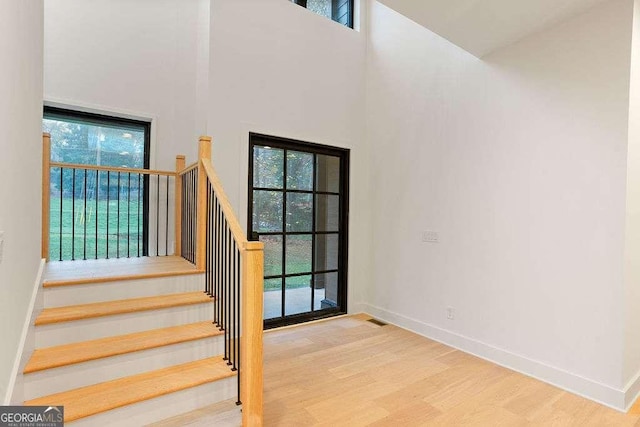 stairway featuring hardwood / wood-style floors, plenty of natural light, and a high ceiling